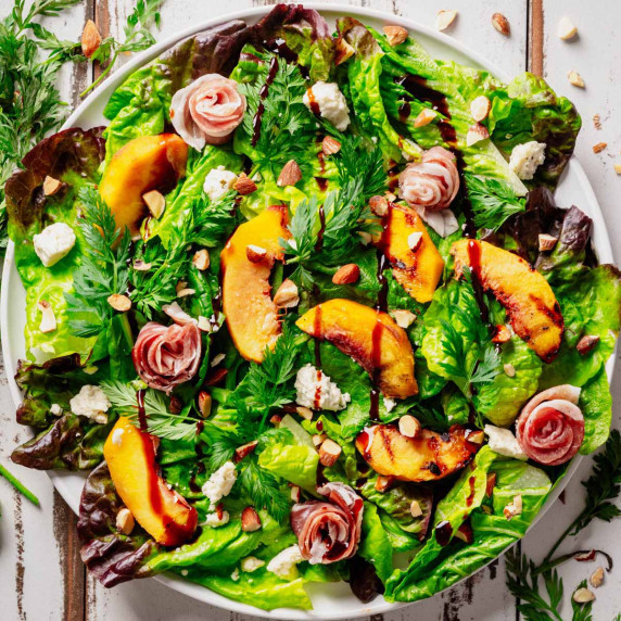 Grilled peach and prosciutto salad with Boursin cheese, toasted almonds, and fresh greens, garnished