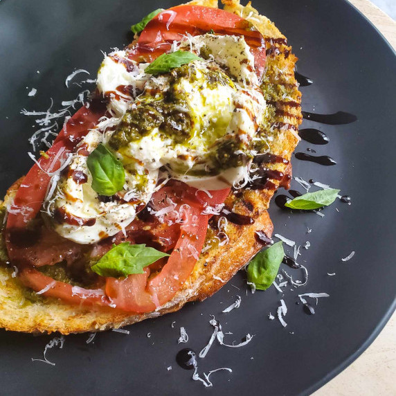 Grilled, golden sourdough topped with fresh ingredients on a black plate.