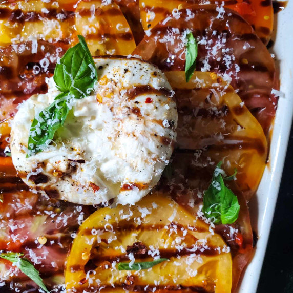 A colourful assortment of tomatoes with white burrata and a black drizzle of balsamic.