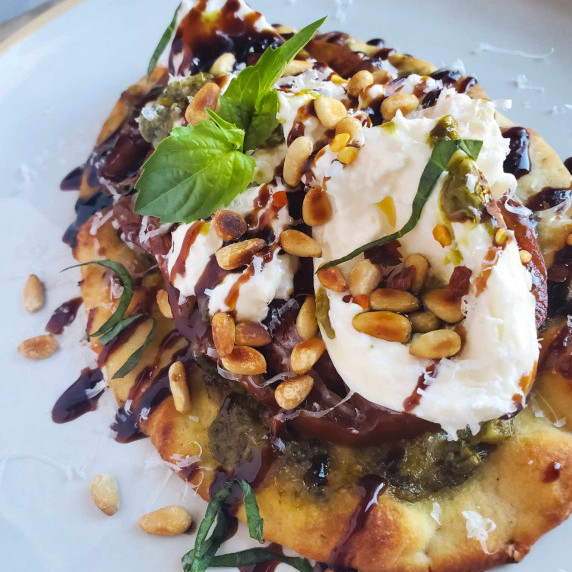 Golden brown naan, green pesto, white burrata, and a black balsamic drizzle.