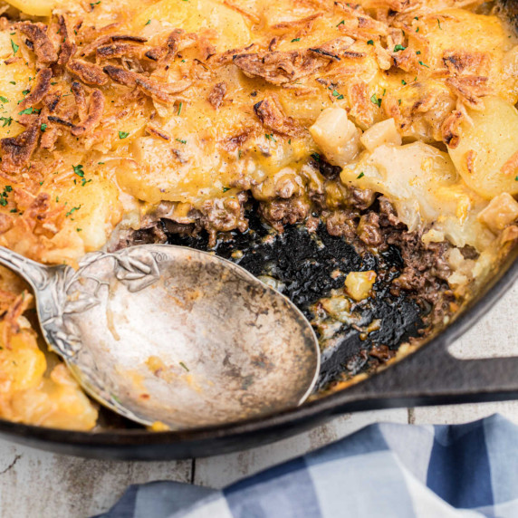Close up inside a skillet with hobo casserole, and a spoon resting where there's some missing.