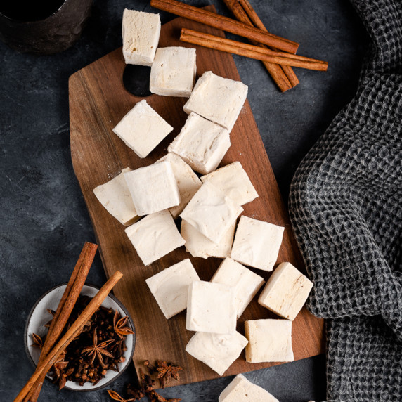 Gingerbread marshmallows arranged on a wooden tray on a dark countertop.