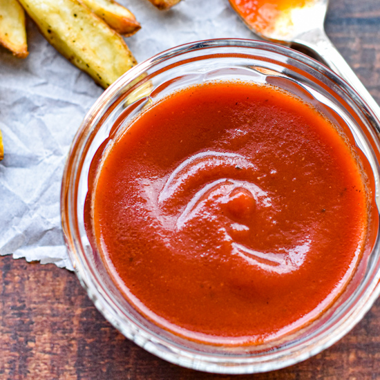 a bowl of homemade ketchup next to some fries and a spoon covered in ketchup
