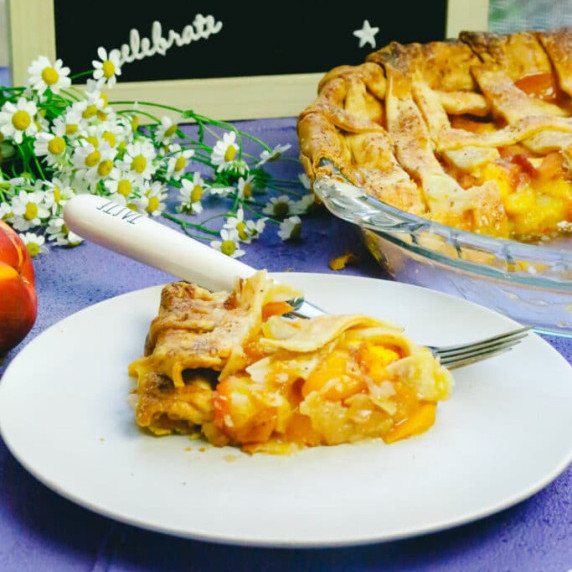 A slice of homemade honey peach pie on a white plate with a fork that says taste 