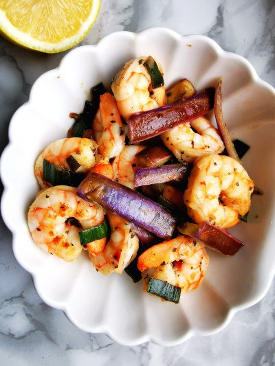 Shrimp, eggplant salad on a white plate with lemon on the side