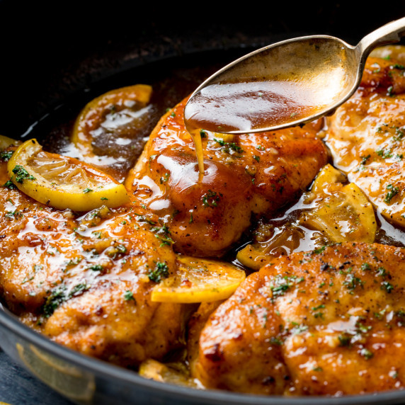 A pan with crispy chicken breast in a honey lemon sauce with slices of lemon.
