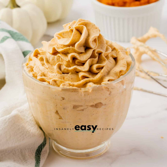 Pumpkin whipped cream in a small glass bowl, with the used whisk at the back