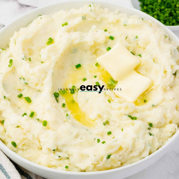 Ranch mashed potatoes with with two cubes of butter and fresh chives in a white bowl