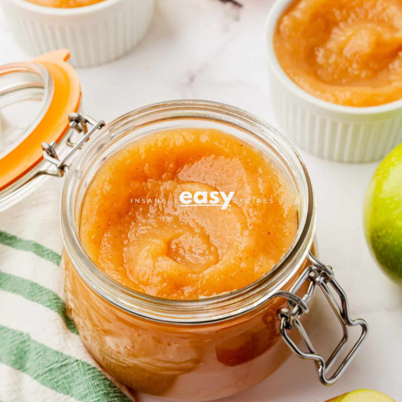 Unsweetened applesauce in a glass jar with a green apple and bowls of the same sauce nearby it