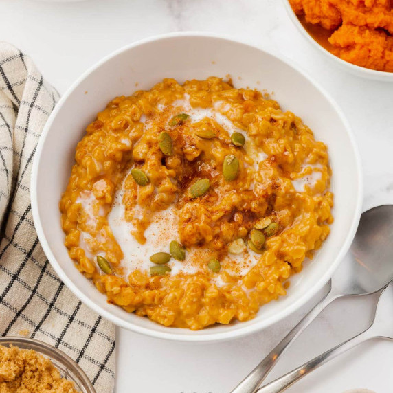 Pumpkin spice oatmeal topped with pepitas, milk, brown sugar, & pumpkin pie spice in a bowl 