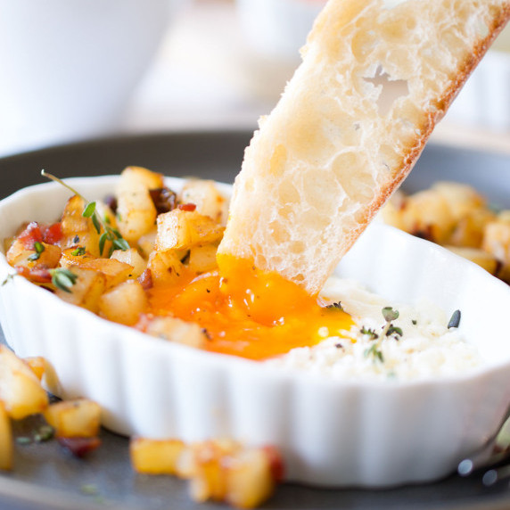Toast being dunked into a baked egg yolk surrounded by hash browns.