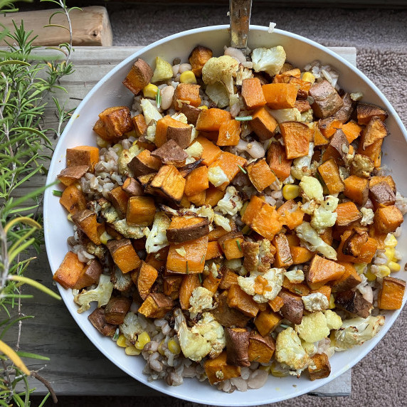 Sweet potatoes in a white bowl with cauliflower, farro and corn on a wood plank