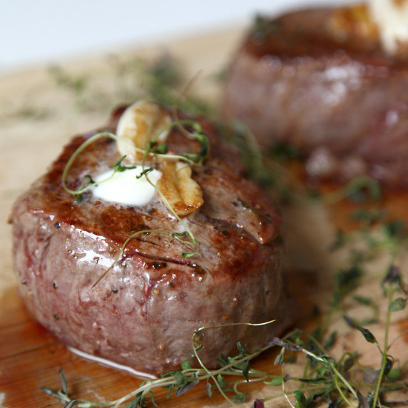Seared grass fed filet mignon with butter, garlic and thyme on a cutting board