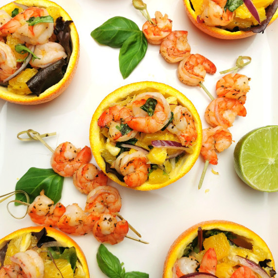 Shrimp salad in orange peel with shrimp skewers, fresh basil and lime on the side