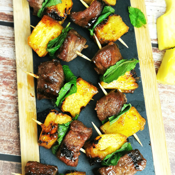 been and pineapple appetizer arranged on a wooden serving platter with pineapple slices on the side