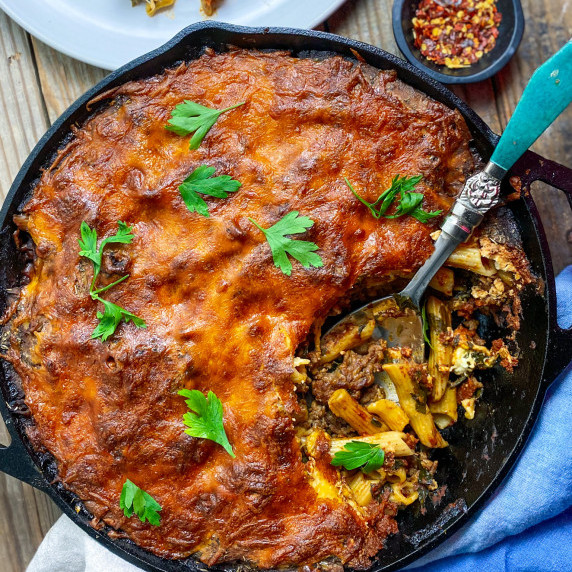 Italian sausage pasta bake in a cast iron pan with a spoon and hot pepper flakes