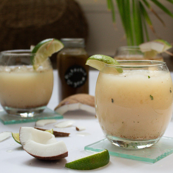 short glasses filled with coconut ginger fizz coconut cocktail with garnishes of lime and coconut 