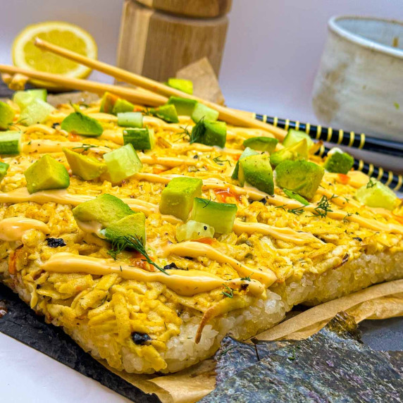 Vegan sushi bake with a tofu crab topping, garnished with diced cucumber, avocados and spicy mayo.