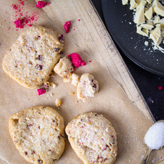 3 white cookies with red specks of fruit lay on cutting board with sprinkles of sugar around