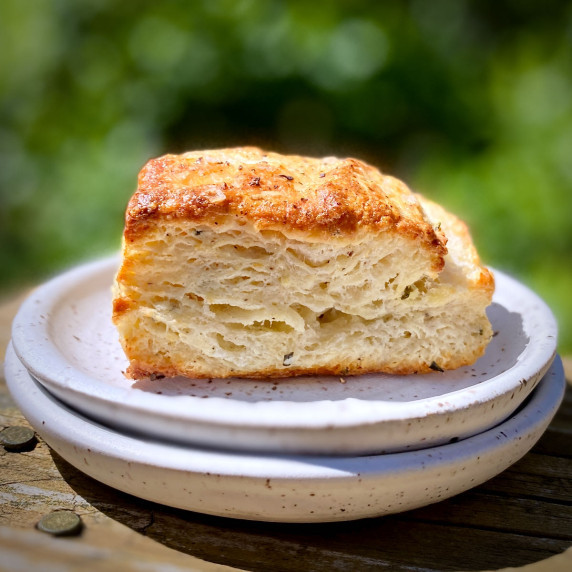 Two small white plates with a single, extra flaky, buttermilk biscuit.