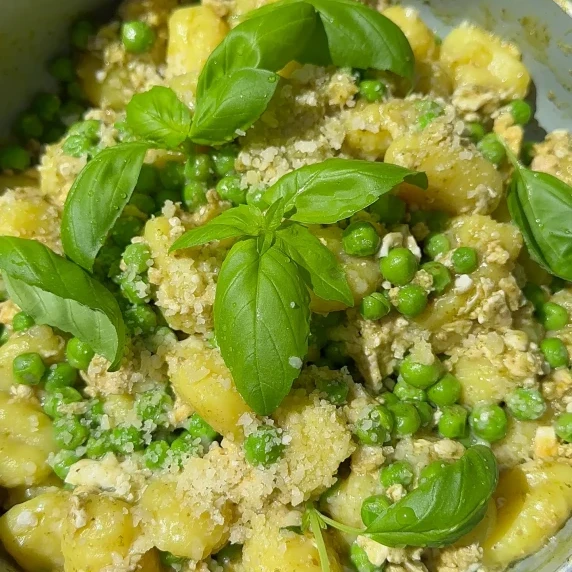 A pan of pesto gnocchi topped with fresh peas and basil, served as a simple and quick dinner. 