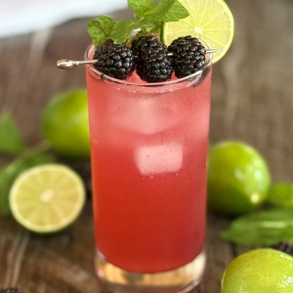 A tall glass filled with a blackberry mojito mocktail is garnished with fresh blackberries and mint.