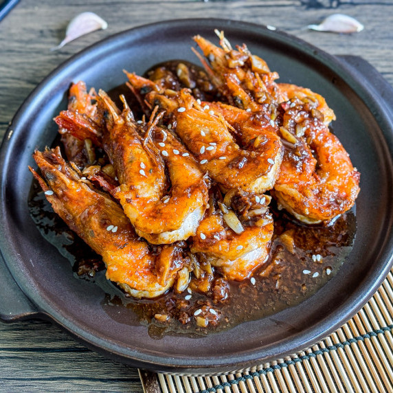 Chinese garlic shrimp with sauce and sesame seeds in a black dish.