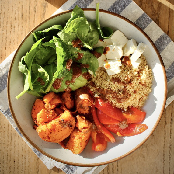 Salad bowl filled with sweet potato, feta, roasted pepper, couscous, spinach and avocado