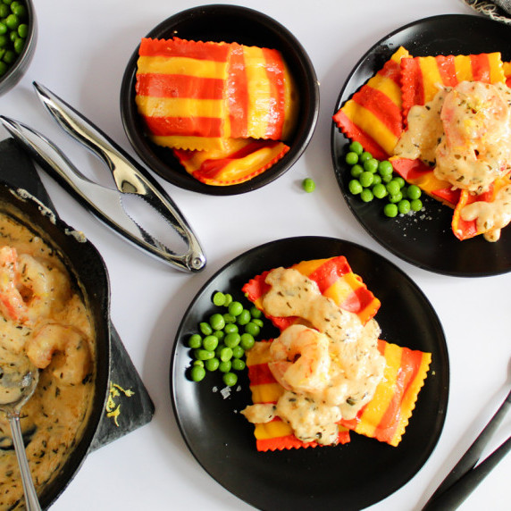 plates with lobster ravioli and cream shrimp sauce, green peas on side.