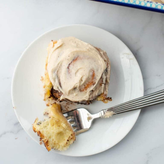 Photo of one chocolate sweet roll with espresso frosting with a bite taken out on a white plate 