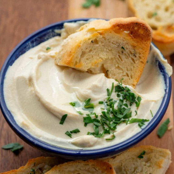 Small bowl of tofu whipped ricotta with truffle oil and parsley garnish surrounded by garlic bread