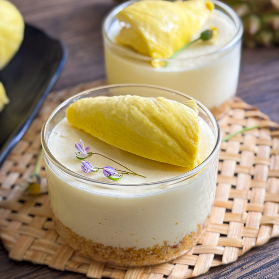 Glass jar of no-bake durian cheesecake topped with fresh durian and edible flowers.
