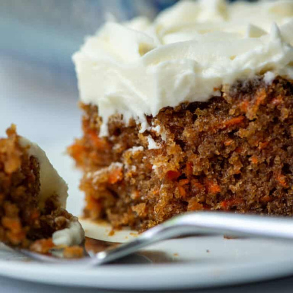 Close up side view photo of a slice of carrot cake with cream cheese frosting on a plate with a fork