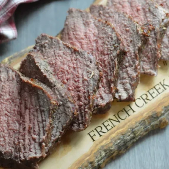 A wooden board that has a rump roast slice thinly on it. The board says “French creek farm”