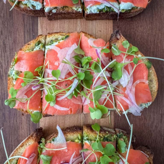 Overhead view of a toasted piece of salmon bruschetta topped with sliced red onions and microgreens 