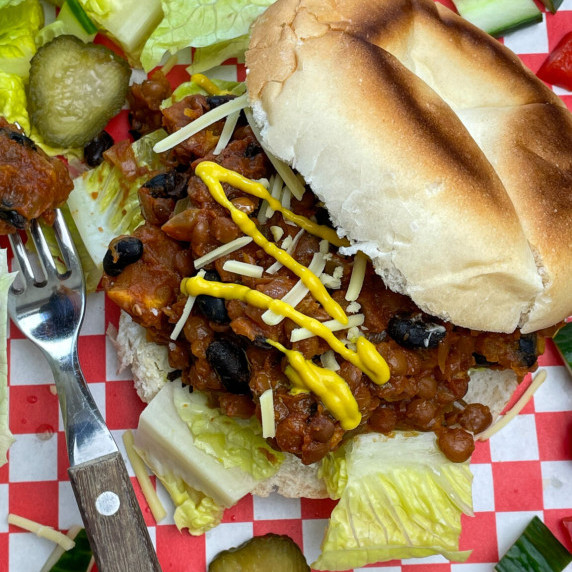 Sloppy joes scooped onto a bread bun with mustard and vegan cheese topping, fork to side.