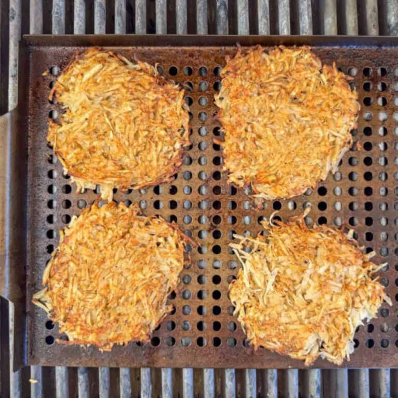 Overhead photo of four hash browns cooking on a grill plate on a gas grill