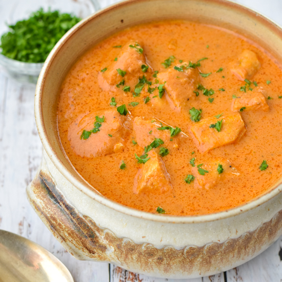 instant pot butter chicken in a beige pottery bowl in front of a bowl of chopped parsley