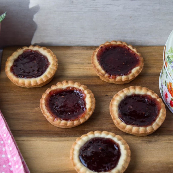 five raspberry jam tarts on a wooden board 