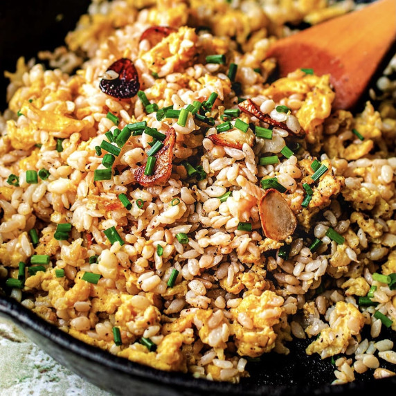 Fried rice, garlic and chives in a cast iron skillet with a wooden spoon