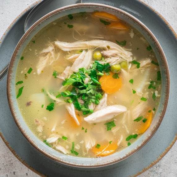 Leftover Turkey Soup in bowl on plate, on marble table.