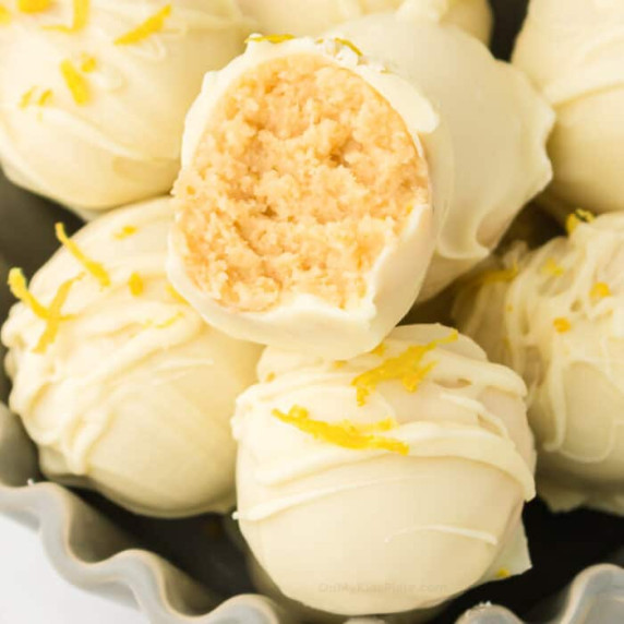 Zoomed in square shot of a lemon truffle with a bite on top of other lemon truffles.