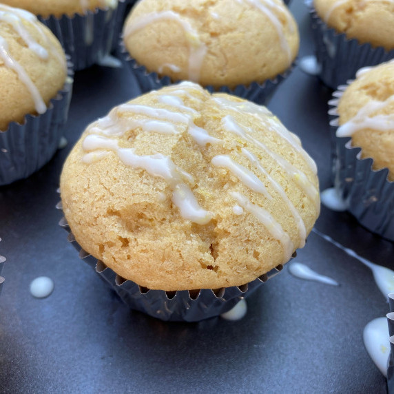 Lemon muffins drizzled with a white glaze on a black cutting board.