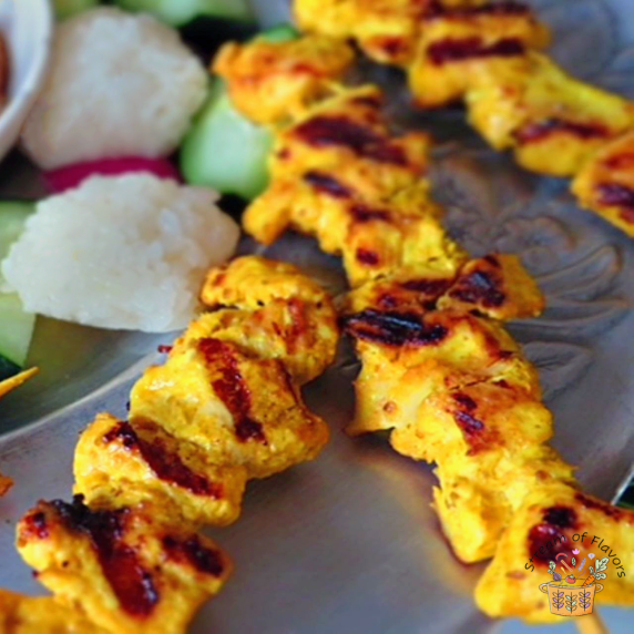 Malaysian Chicken Satay with rice cakes and cucumber on a metal plate with peanut sauce