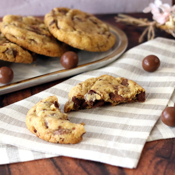 Malted milk chocolate cookies on a platter, single broken cookie in front on a napkin