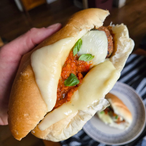 A soft roll filled with red pesto, white mozzarella, pops of green basil, and meatballs.