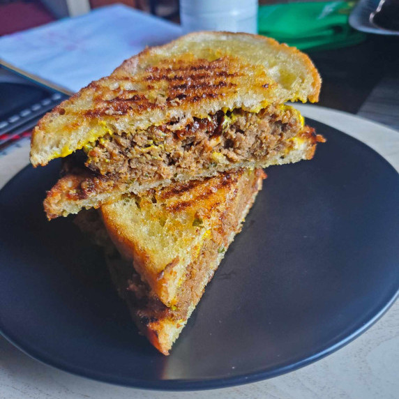 Meatloaf wedged between two golden brown pieces of bread on a black plate.