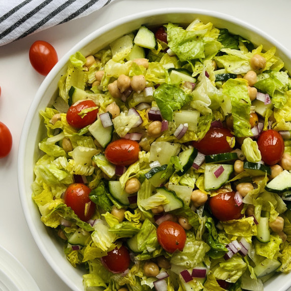 Tossed salad of lettuce, tomato, cucumber and onion in a white bowl on a white countertop.