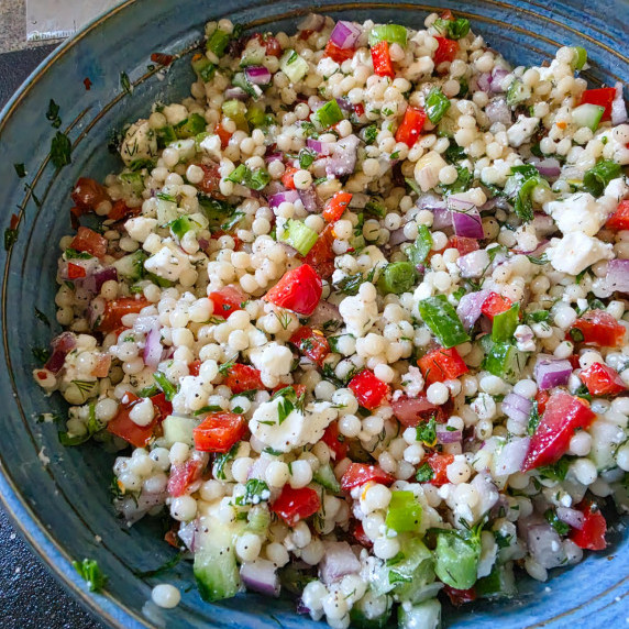 A blue bowl full of couscous and vibrant, colourful veggies & herbs.