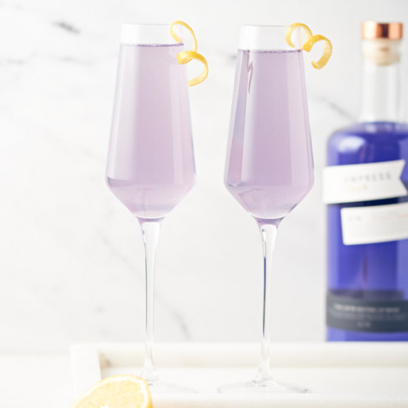 side view of 2 glasses filled with cocktail with bottle of gin in background on marble